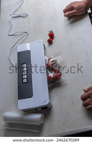 a man's hand is using a vacuum machine to vacuum pack strawberries into plastic bags. 