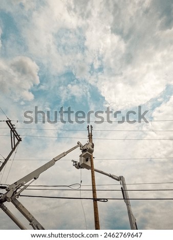 Lineman Prepare to Work on the Power Supply Line. Lineman crews work on power lines high in the sky. An elevated hydraulic bucket lifts the workers up to the power line. Morning views.