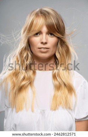 A close-up portrait of a young woman with wavy blonde hair, wearing a simple white top. Modern and natural look, fashion and beauty industry, studio photography.