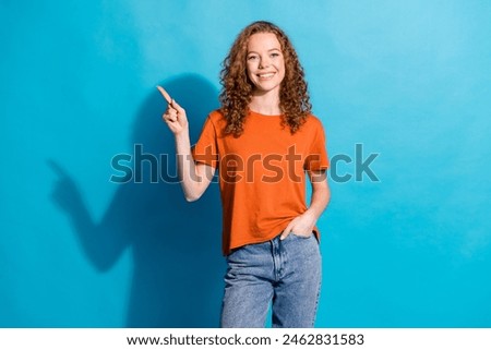 Photo of cheerful red haired youngster student girl in orange t shirt and jeans directing finger new outfits store isolated on blue color background