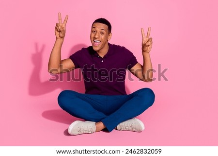 Full length photo of nice young male sit floor show v-sign dressed stylish violet garment isolated on pink color background