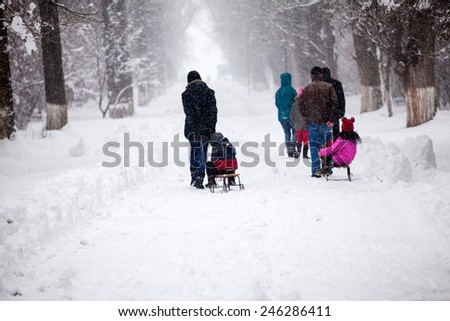Snowing landscape in the park with people passing by with sledges