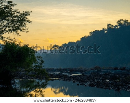 The serene beauty of a tranquil river at sunrise, with silhouetted trees lining its banks, creating a picturesque natural landscape.