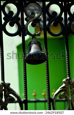 A bell made of brass with a classic and unique shape that appears to be installed in the middle of the entrance to the iron fence of the house