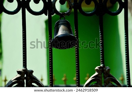 A bell made of brass with a classic and unique shape that appears to be installed in the middle of the entrance to the iron fence of the house