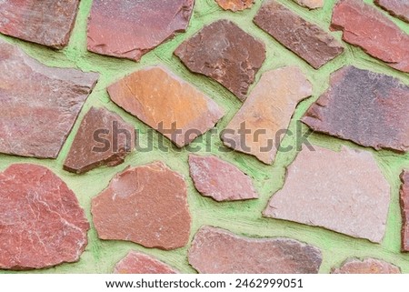 It is view of colorful stones on green background. Its close up view of mosaic stone wall of building. It is photo of multicolored stone tile floor