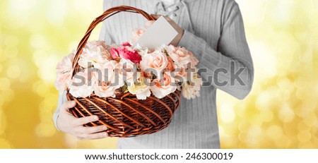 holidays, people, feelings and greetings concept - close up of man holding basket full of flowers and postcard over yellow lights background