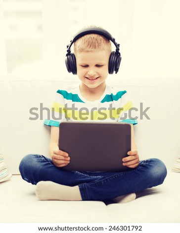 home, childhood, leisure, technology and music concept - smiling little boy with tablet pc computer and headphones at home