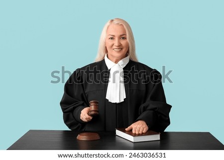 Mature female judge with gavel and book at table on blue background