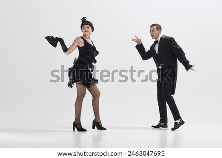Elegant woman and man in retro attire engage in fun, choreographed dance, evoking the spirit of bygone era isolated over white studio background. Concept of art, retro and vintage, entertainment, 20s