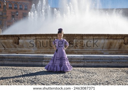 Girl dancing flamenco, posing looking at camera, in typical flamenco costume next to spectacular fountain in a beautiful square in Seville. Dance concept, flamenco, typical Spanish, Seville, Spain. Royalty-Free Stock Photo #2463087371