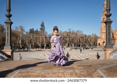 Girl dancing flamenco, twirling to show off her costume, in typical flamenco dress on a bridge in a beautiful square in Seville. Dance concept, flamenco, typical Spanish, Seville, Spain. Royalty-Free Stock Photo #2463087379