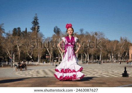 Girl dancing flamenco, posing looking at camera, in typical flamenco dress on a bridge in a nice square in Seville. Dance concept, flamenco, typical Spanish, Seville, Spain. Royalty-Free Stock Photo #2463087627