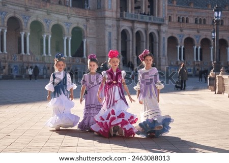 Four girls dancing flamenco, walking, in typical flamenco dress in a nice square in Seville. Dance concept, flamenco, typical Spanish, Seville, Spain. Royalty-Free Stock Photo #2463088013
