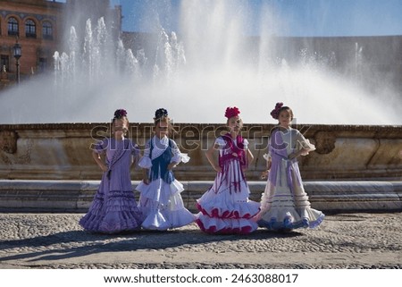 Four girls dancing flamenco, posing looking at camera, wearing typical flamenco costumes next to a spectacular fountain in a beautiful square in Seville. Dance concept, flamenco, typical Spanish. Royalty-Free Stock Photo #2463088017