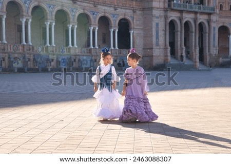 Two girls dancing flamenco walking and talking happily, with typical flamenco dress in a nice square in Seville. Dance concept, flamenco, typical Spanish, Seville, Spain. Royalty-Free Stock Photo #2463088307