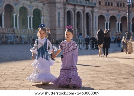 Two girls dancing flamenco walking and talking happily, with typical flamenco dress in a nice square in Seville. Dance concept, flamenco, typical Spanish, Seville, Spain. Royalty-Free Stock Photo #2463088309