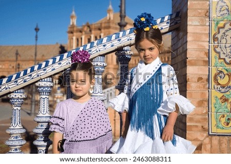 Two girls dancing flamenco posing looking at camera in typical flamenco costumes on stairs in a beautiful square in Seville. Dance concept, flamenco, typical Spanish, Seville, Spain. Royalty-Free Stock Photo #2463088311