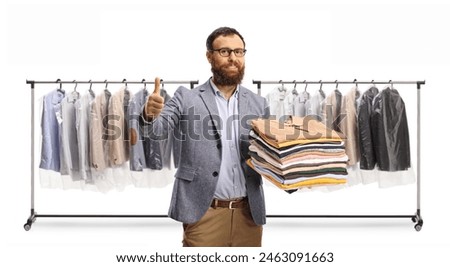 Man gesturing thumbs up in front of a rack with hanging clothes isolated on a white background