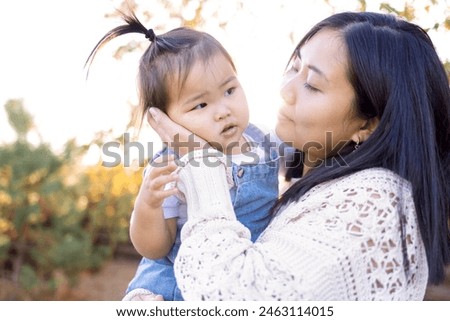 A young Asian woman hugs her little daughter. An attractive mom walks with her cute girl outdoors. Happy Korean family in the park.