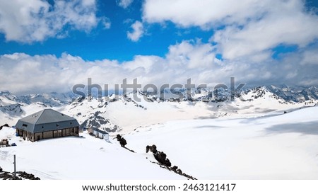 The snow-covered mountain peaks, the cozy cabin, and the clear blue sky create a serene and picturesque scene. Royalty-Free Stock Photo #2463121417