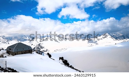 The snow-covered mountain peaks, the cozy cabin, and the clear blue sky create a serene and picturesque scene. Royalty-Free Stock Photo #2463129915