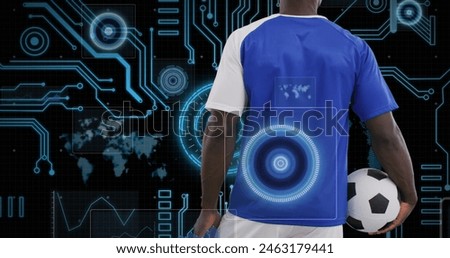 Man in blue jersey holding soccer ball, standing before digital interface. He examining futuristic soccer analytics, technology enhancing sports strategy