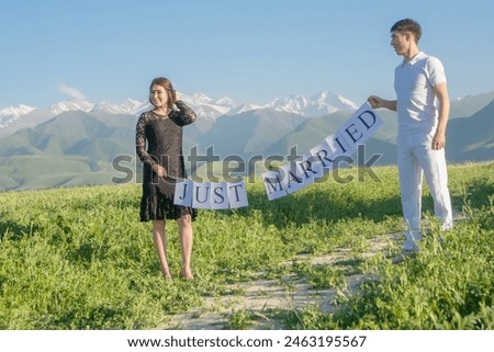 a guy and a girl of Asian nationality Kyrgyz in nature, against the backdrop of the mountains. holding a sign, banner newlyweds, newlyweds