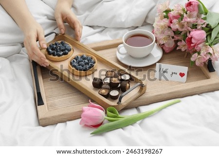 Tasty breakfast served in bed. Woman with desserts, tea, flowers and I Love You card at home, closeup
