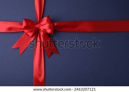 Red satin ribbon with bow on blue background, top view