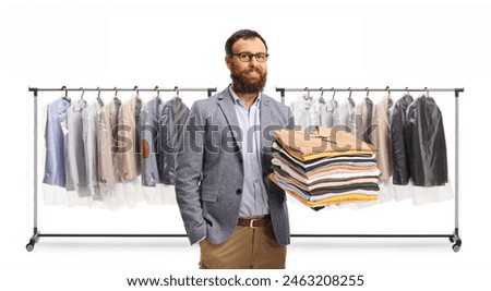 Man holding a pile of folded clothes in front of a rack with clothes on hangers isolated on a white background