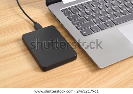 External backup hard disk drive connected to laptop on wooden table. external hard disk connect by USB 3.0 port to laptop