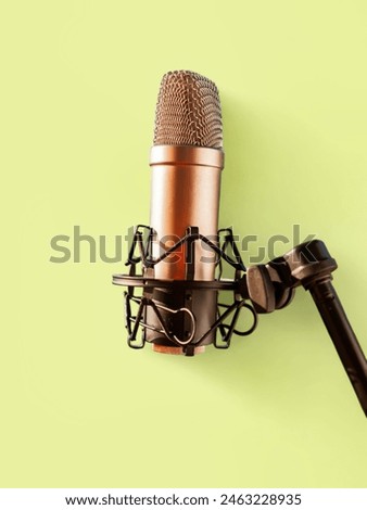  A condenser microphone with a shock mount attached to a boom arm, set against a solid light green background. This professional audio recording equipment is commonly used in podcasting, music product