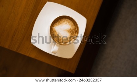 A cup of latte coffee with a picture of a heart is served hot on the table