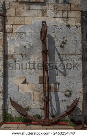 Big old rusted anchor resting again stone wall.
