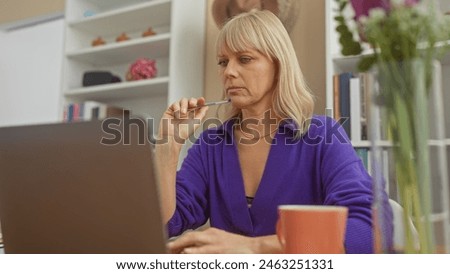 Pensive blonde woman working from home with a laptop in a cozy living room setting.