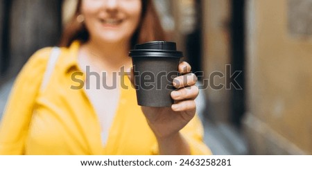 Woman gives paper black coffee cup or tea on urban background. Take away or delivery concept. Copy space. Place for your text on mug, mockup.