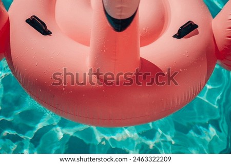A pink inflatable flamingo is floating in a pool. The water is clear and calm. The flamingo is the main focus of the image, and it is enjoying its time in the water