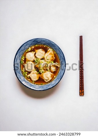  A top view of a delightful bowl of wonton soup, showcasing traditional Asian cuisine. The blue bowl is filled with delicious dumplings in a clear broth, garnished with fresh greens