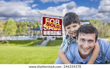 Mixed Race Father and Son Celebrating with a Piggyback in Front Their House and Sold Real Estate Sign.