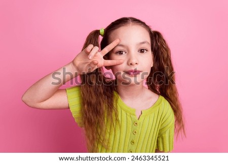 Photo portrait of cute little girl show v-sign posing dressed stylish green clothes isolated on pink color background