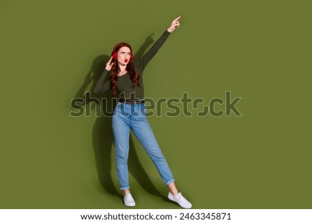 Full length photo of shiny attractive lady earphones dressed shirt having fun pointing empty space isolated green color background