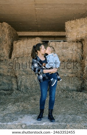 Mom kisses a little girl in her arms standing in the hayloft