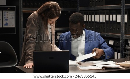 Multiethnic private detectives collaborate in incident room, conducting criminal investigation. African american and caucasian inspectors collecting clues and information using, laptop and case files. Royalty-Free Stock Photo #2463355145