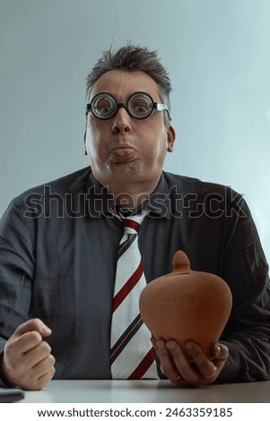 Awkward man in a dark gray shirt and striped tie, with spiky gray hair and oversized round glasses, holds a piggy bank, representing poor money management skills, plain background