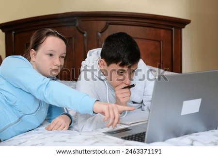 Two caucasian children watching something funny on laptop. Attractive brunette boy pointing his hand on screen. Pretty little girl laughing from what she see on computer. High quality 