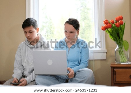 Two caucasian children watching something funny on laptop. Attractive brunette boy pointing his hand on screen. Pretty little girl laughing from what she see on computer. High quality 