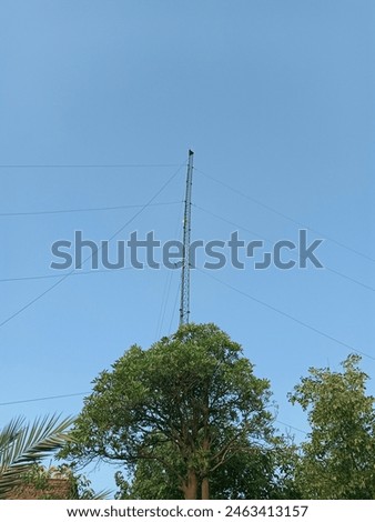 "Wireless tower rises against a backdrop of vivid blue sky and lush greenery, symbolizing connectivity amidst natural serenity. Modern technology meets nature's beauty."