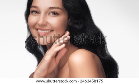 A cheerful portrait of a woman with radiant skin and dark hair, smiling warmly against a white background. Perfect for beauty, skincare, and wellness projects.