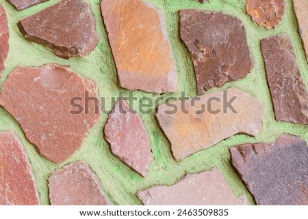 It is the view of colorful stones on green background. Its close up view of mosaic stone wall of building. It is photo of multicolored stone tile floor